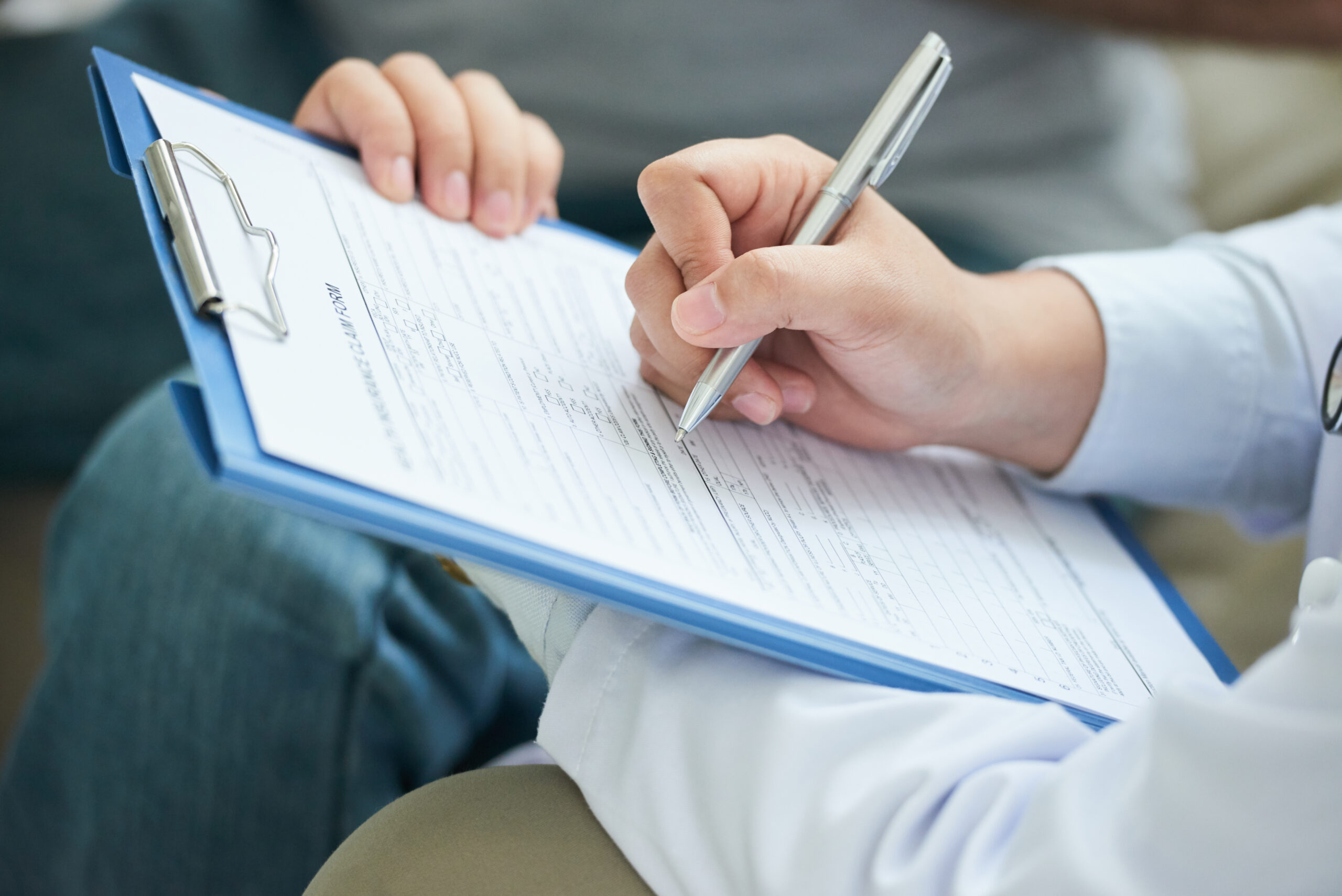 Crop shot of anonymous doctor in white gown writing with pen on clipboard during home visit